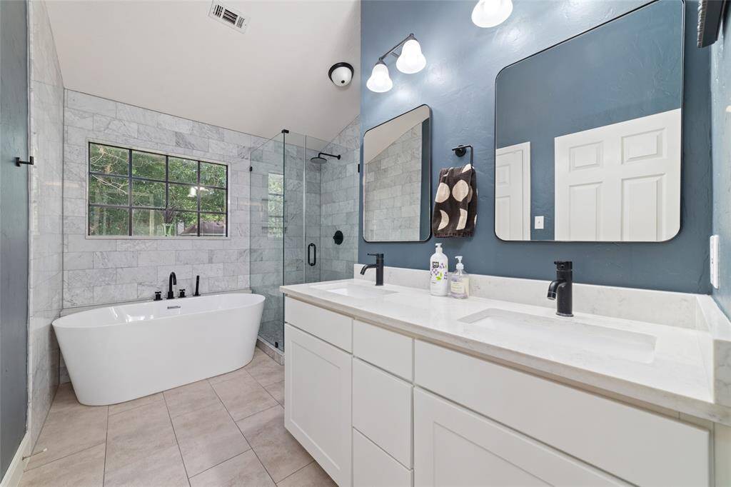 Completely updated primary bathroom with double sink vanity, freestanding soaking tub, and frameless glass shower. Spacious 11x4 walk-in-closet to the left.