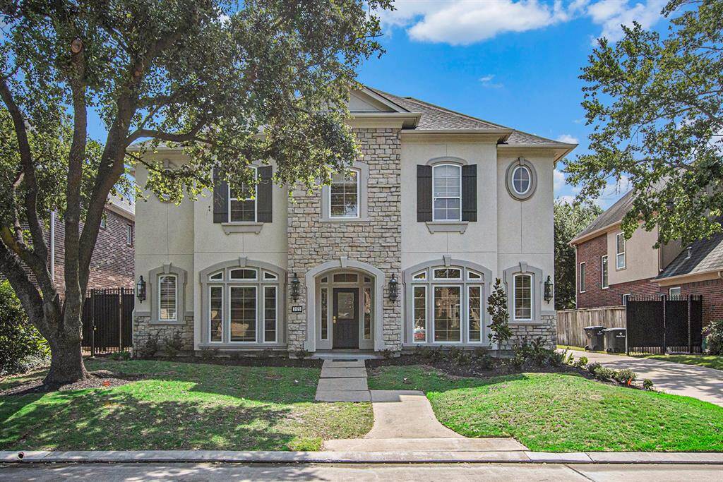 This charming two-story home features a classic stone and stucco facade with elegant arched windows. The neatly landscaped front yard includes mature trees, creating an inviting curb appeal. A spacious driveway leads to a secure side gate, enhancing privacy and accessibility.