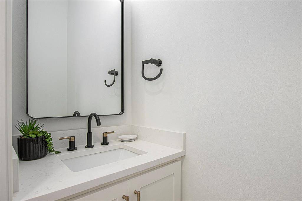Modern half bath downstiars has a sleek white vanity, black fixtures, and a rectangular mirror.