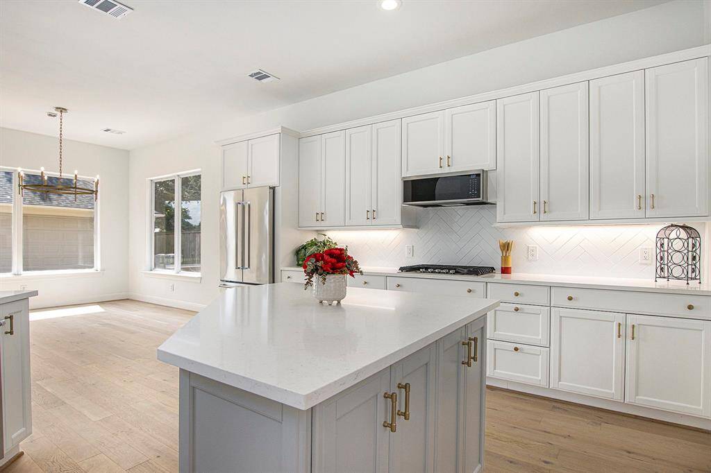 This kitchen features a bright, open design with ample natural light. It has modern white cabinetry, all brand new stainless steel appliances, and a large island with a sleek quartz countertop.