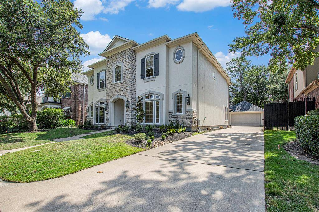 This home has a well-maintained front lawn, freshly mulched garden beds, a long driveway leading to a detached garage, and mature trees providing shade.