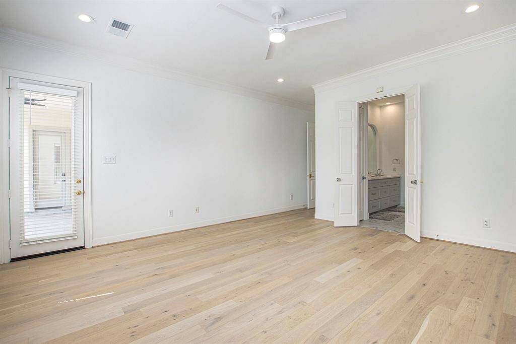 This bright, spacious room features light wood floors, white walls, and recessed lighting, creating an inviting atmosphere. It includes a ceiling fan, access to a private patio, and an en-suite bathroom with double doors for added convenience.