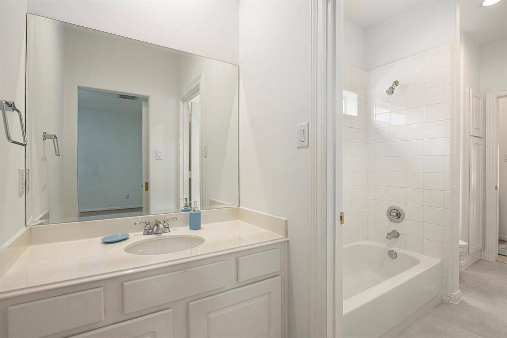 This bathroom features a large mirror, single-sink vanity, and a tiled shower-tub combination