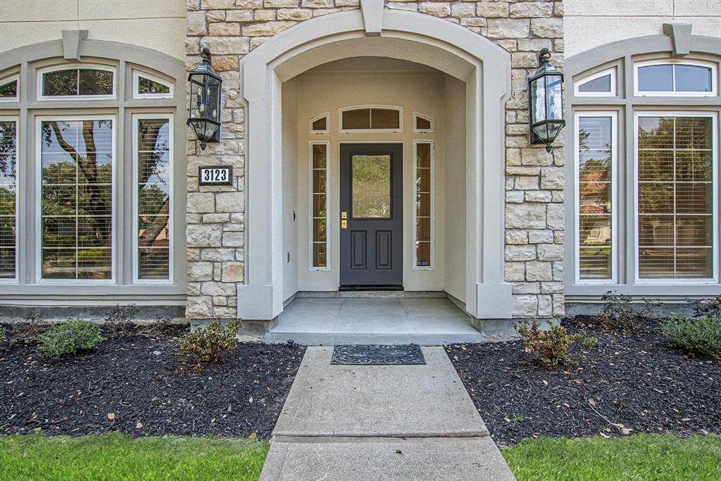 The elegant home entrance has a welcoming front door framed by stone accents and large windows. Well-maintained landscaping lines the walkway, enhancing curb appeal.
