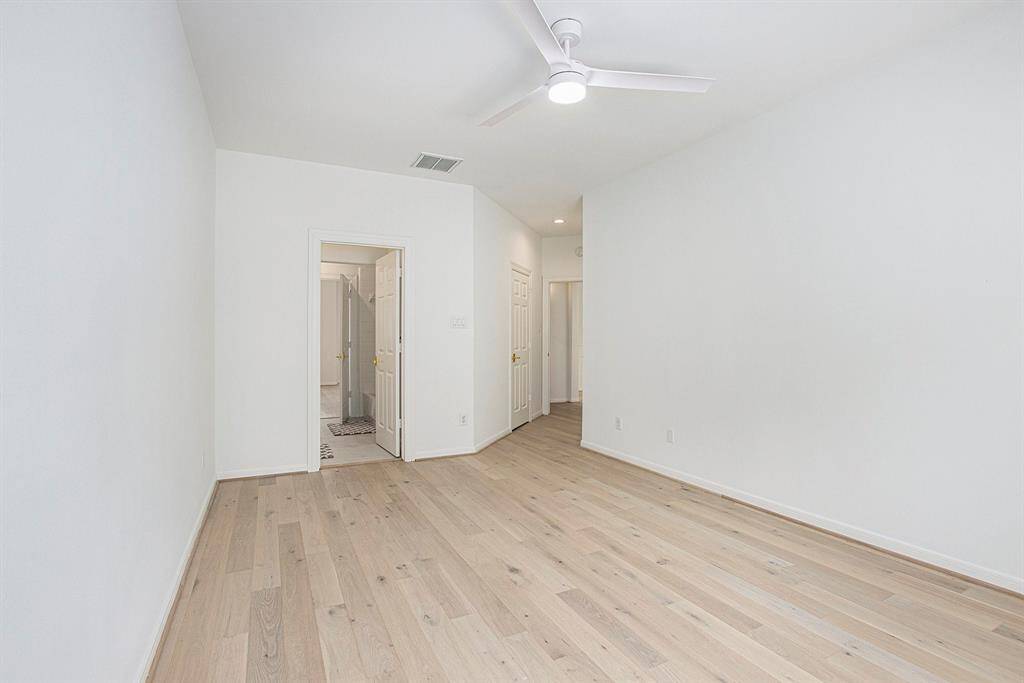 A reverse view of the room shows again the light wood floors, white walls, modern fan, and ensuite bathroom.