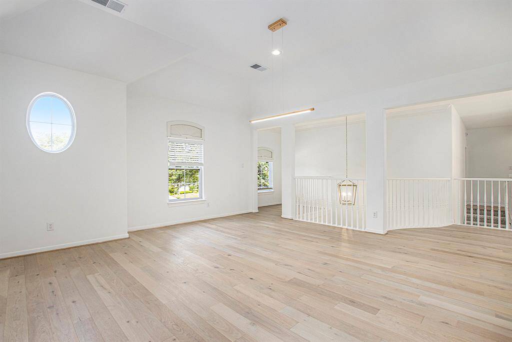 This is the enormous gameroom featuring a unique circular window and a modern pendant light. Large, arched windows provide natural light, and an open railing overlooks the space below, adding to the open feel.