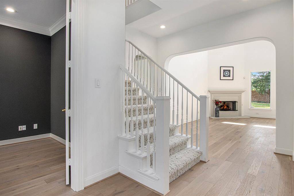 Bright entryway with a modern staircase with brand new stylish carpet, and a view into the spacious living room featuring a cozy fireplace and large window with backyard views.