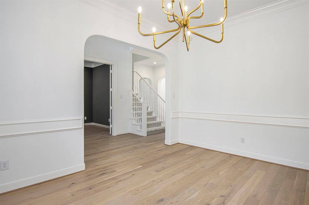 This is a reverse view of the formal dining room. It features elegant wainscoting and a modern gold chandelier. An arched doorway leads to a carpeted staircase, adding charm and character to the space.