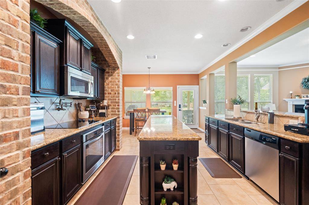 Impressive chef’s kitchen with rich cabinetry, granite counters, and a striking brick arch over the cooktop, all overlooking the bright breakfast area.