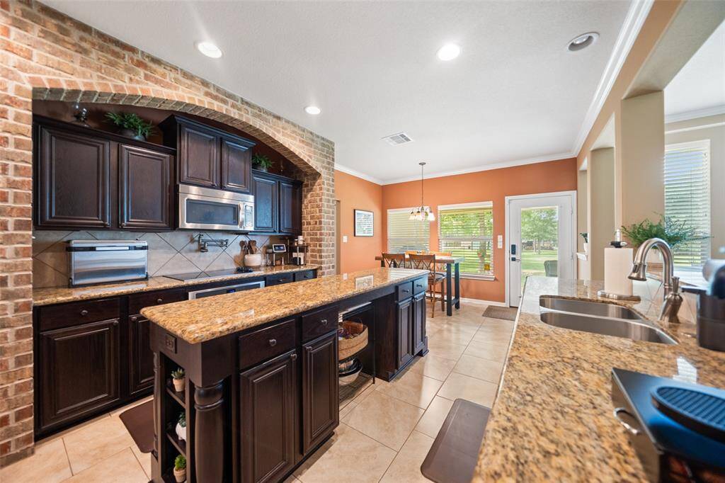 An expansive island anchors this gourmet kitchen, offering plentiful prep space, display shelving, and stainless steel appliances for modern function.