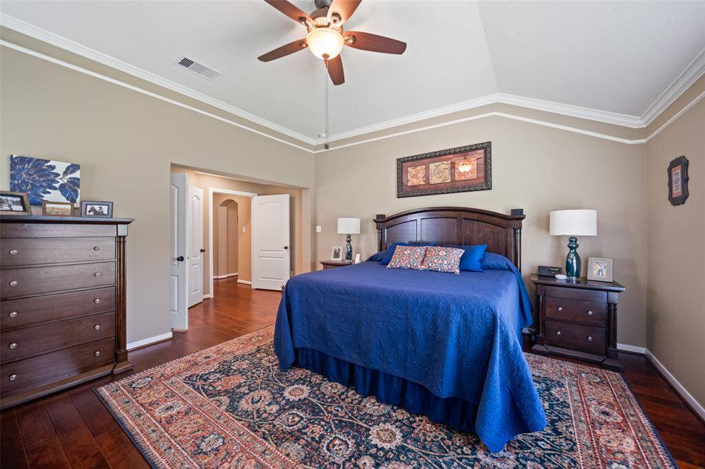 Elegant primary suite with crown molding, wood floors, and ample space for a full furniture set, creating a calm and refined retreat.