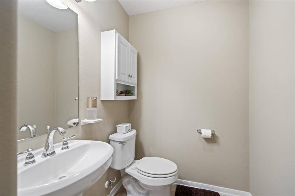 Bright and efficient half-bath featuring a pedestal sink, wall-mounted storage, and neutral tones for a clean, modern feel.