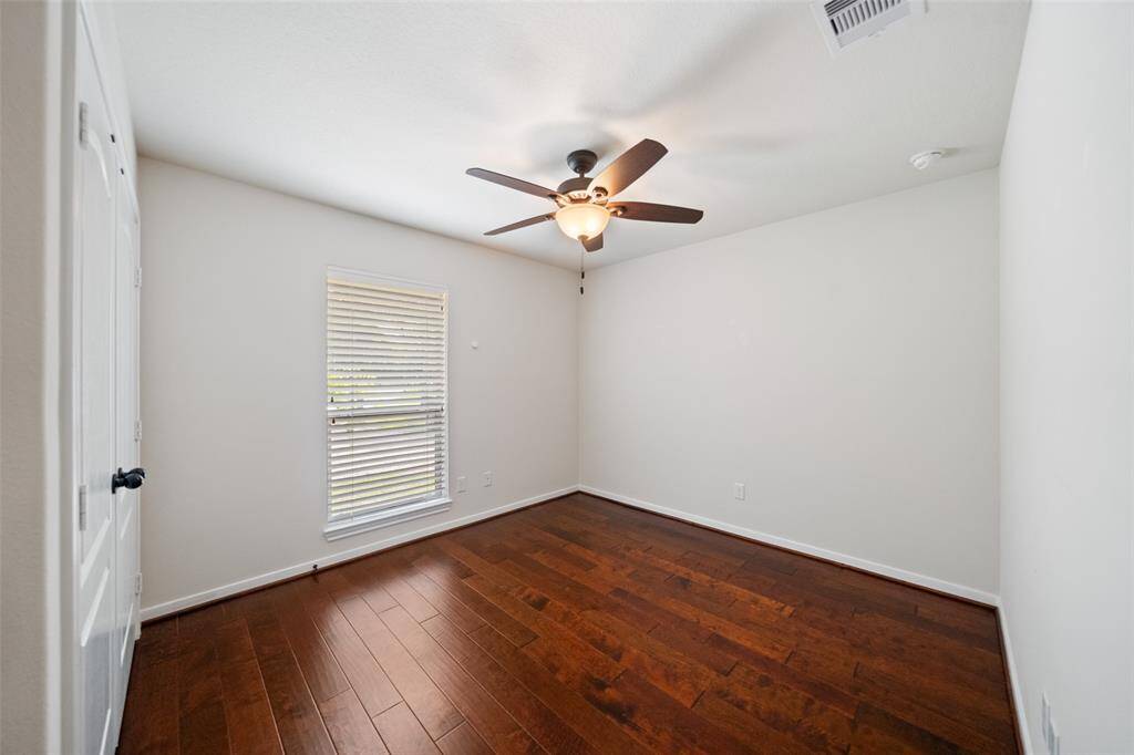 Comfortable secondary bedroom with hardwood flooring, ceiling fan, and a large window offering backyard views and natural light.