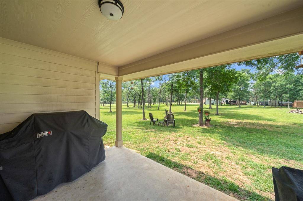 Covered back patio provides a shaded space for outdoor grilling and relaxation, with views of the expansive, tree-dotted yard.