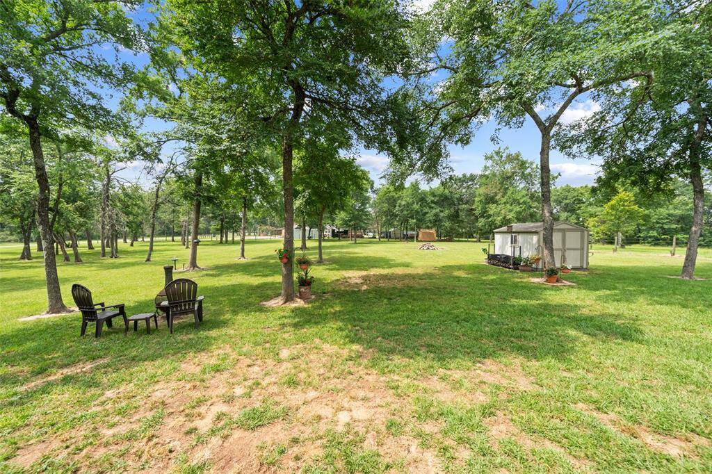 Serene backyard retreat features mature trees, a fire pit with Adirondack seating, and plenty of space to enjoy nature.