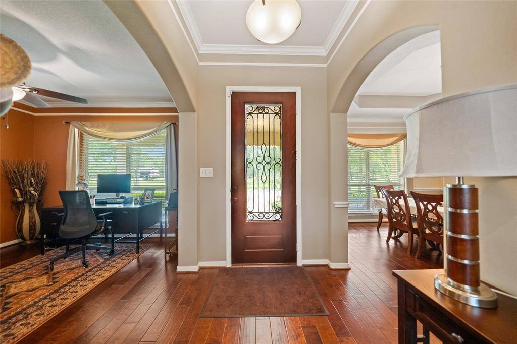 Inviting front entry with a decorative glass door, tray ceiling, and archways leading to the formal dining and office areas.