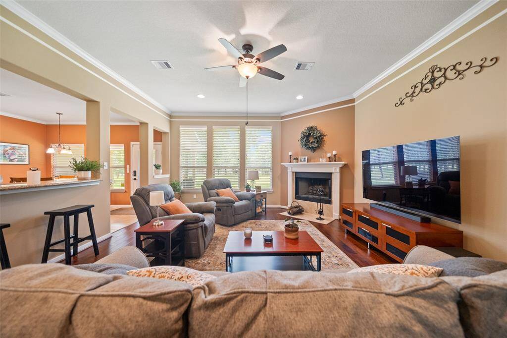 This inviting living area is bathed in light from multiple windows and includes a fireplace, crown molding, and open views into the kitchen and breakfast area.