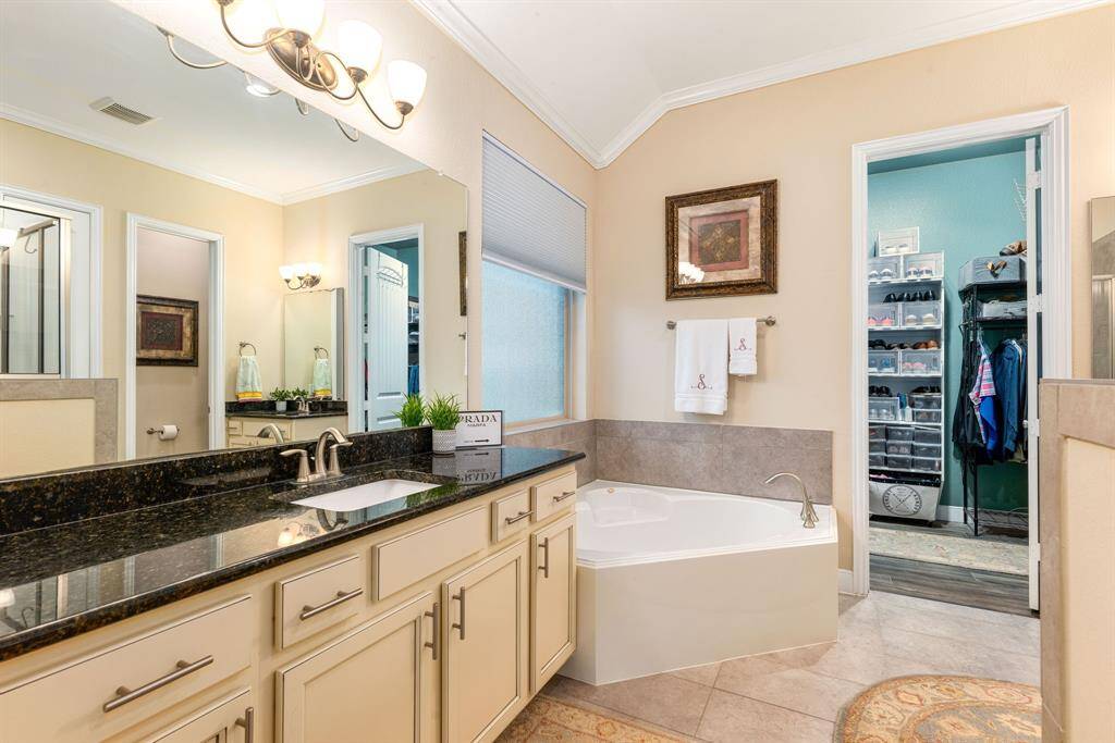 This primary bathroom is definitely move-in ready! Featuring a separate garden tub for soaking after a long day with custom tile detailing, light cabinets with dark countertops, spacious walk-in closet with shelving, high ceilings, custom paint, crown molding and sleek finishes.