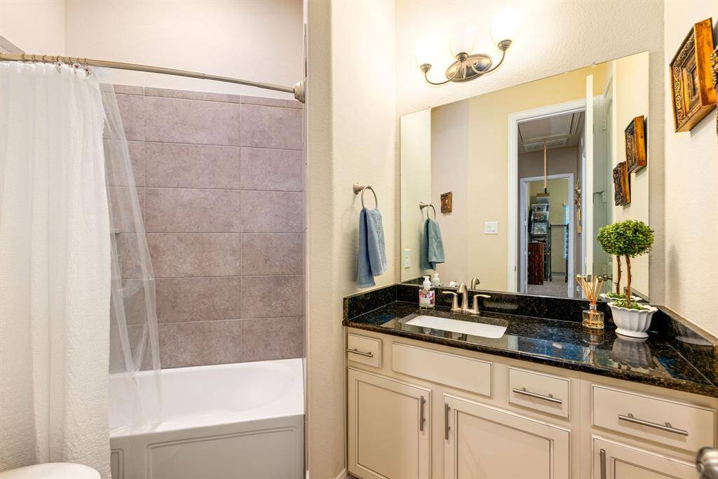 Secondary bathroom features dark countertops and light cabinets, custom neutral paint, shower/tub combo with tile surround, large mirror, tile floors, sleek fixtures and plenty of space to accommodate any visiting family or guests.