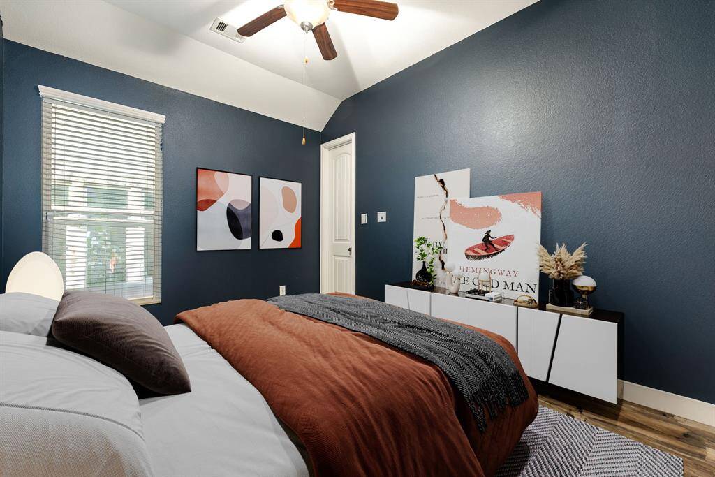 Secondary bedroom features wood like flooring, custom paint, dark stained ceiling fan with lighting and a large window with privacy blinds. *virtual staging*