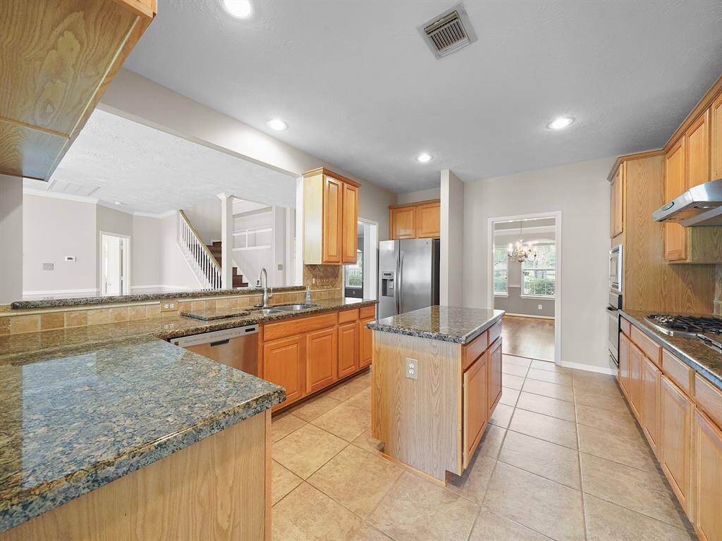 Open kitchen complete with island, stainless steel appliances, granite countertops, and tile backsplash.