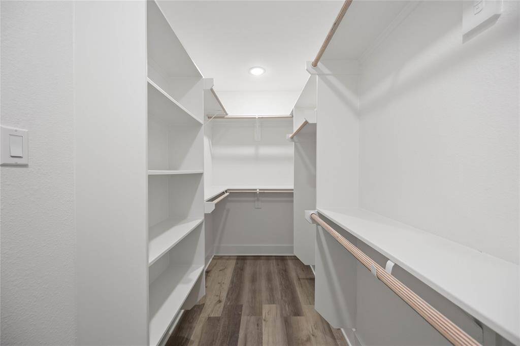 A spacious walk-in closet with plenty of  shelving and hanging space, finished with a clean, modern design and luxury vinyl flooring.