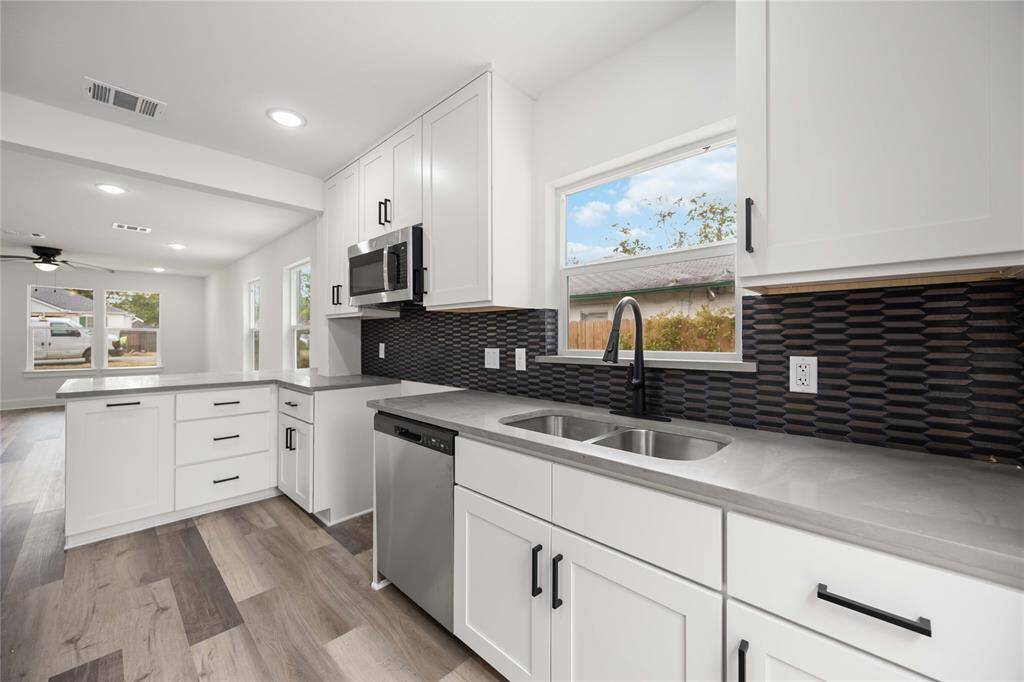 This kitchen includes stainless steel appliances, a unique black backsplash, and an expansive window sitting over the kitchen sink.