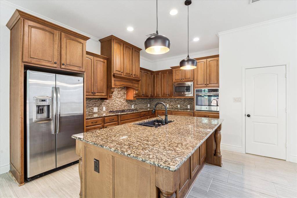 Gourmet kitchen with rich wood cabinetry, granite island, sleek backsplash, and stainless steel appliances—style meets function!