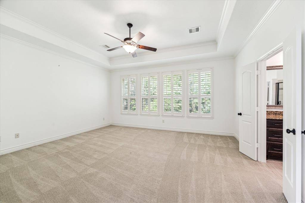 Spacious primary suite featuring tray ceilings, abundant natural light through plantation-shuttered windows, and direct access to a luxurious en-suite bath.