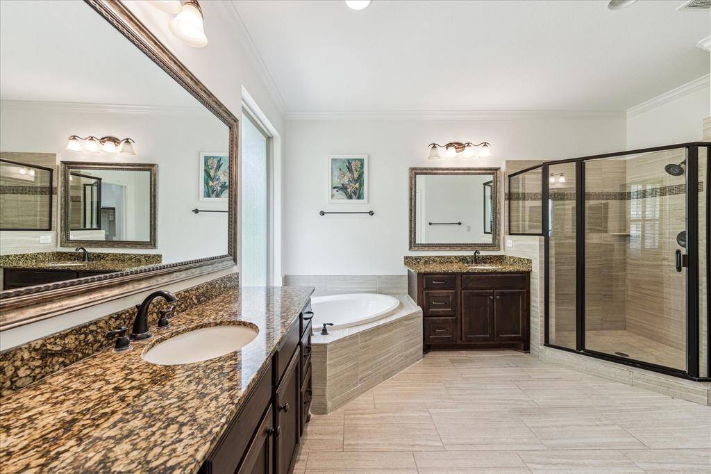 Luxurious primary bath featuring dual granite vanities, a relaxing soaking tub, expansive walk-in shower, and rich wood cabinetry—all accented by elegant tile flooring.
