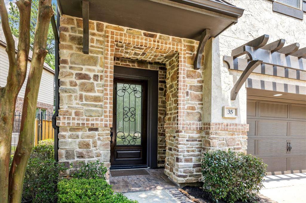 Charming stone entryway with intricate brick detailing, showcasing a stately wrought-iron accented glass door beneath a sheltered archway.