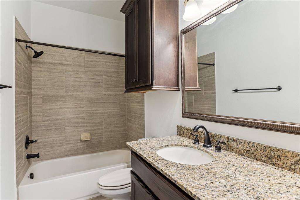 Secondary bath with granite vanity, dark wood cabinetry, and tiled tub/shower combo.