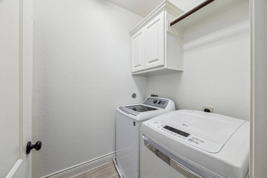Upstairs laundry room featuring upper cabinetry, hanging rod, and modern washer and dryer set.