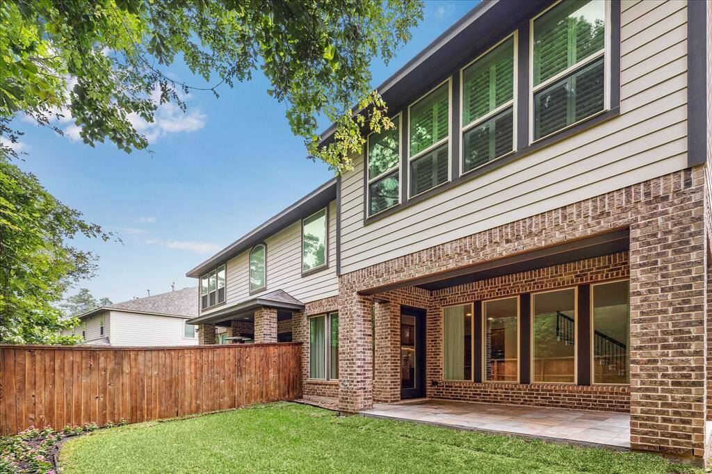 Private fenced backyard with a spacious covered patio, beautifully finished with tile flooring and surrounded by mature trees for added shade and privacy. The home’s brick and siding exterior provides a modern yet timeless look.