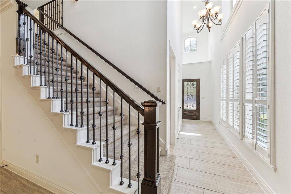 Bright and inviting entryway featuring soaring ceilings, elegant tile flooring, and a wrought-iron front door. A grand staircase with wrought-iron spindles adds a timeless touch.
