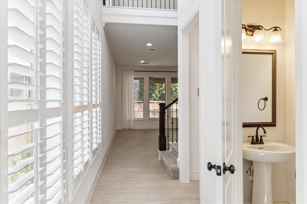 Bright entry hall with plantation shutters, tile flooring, and view into the open living area. Features a stylish powder bath and iron-accented staircase.