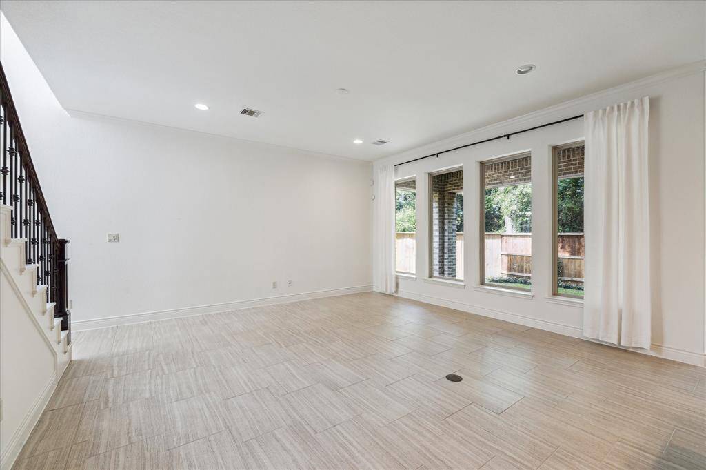 Spacious living room with tile flooring, recessed lighting, and wall of windows offering natural light and backyard views.