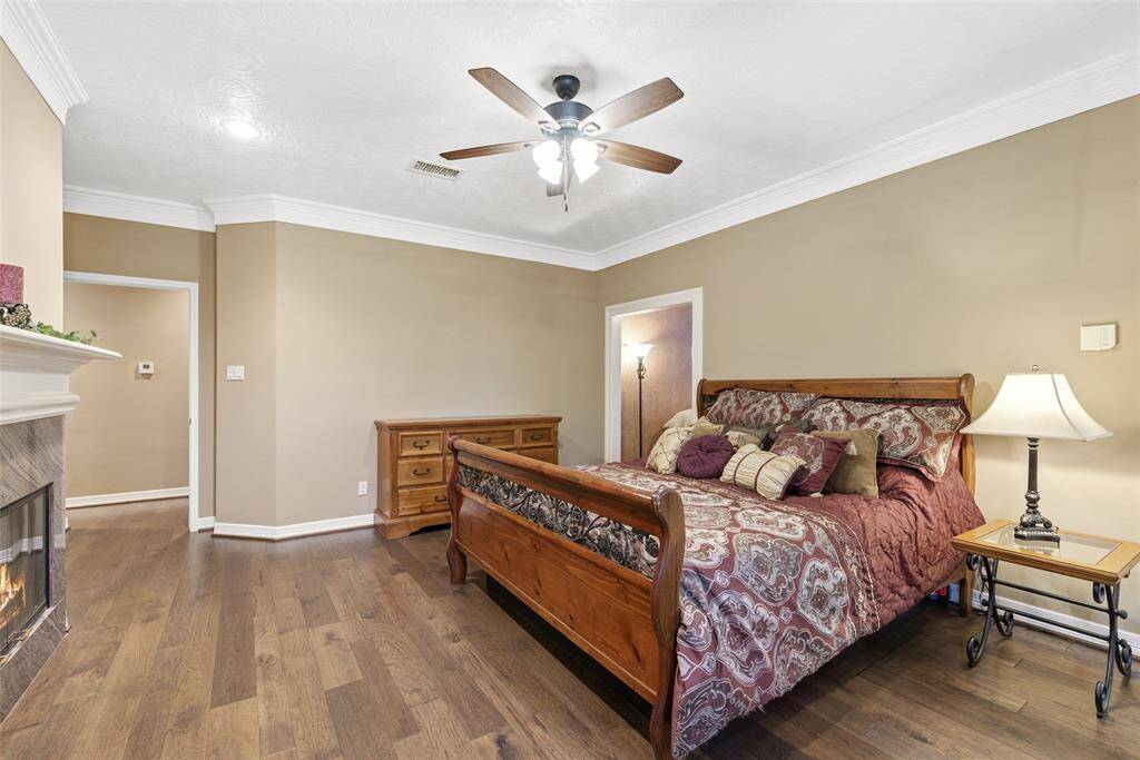 Primary bedroom features a warm color palette, hardwood floors, and a decorative fireplace. The room is spacious and inviting, perfect for relaxation.