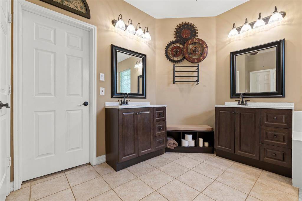 The primary bathroom features a dual vanity with dark wood cabinets, large mirrors, and modern lighting. The neutral tile flooring complements the beige walls.