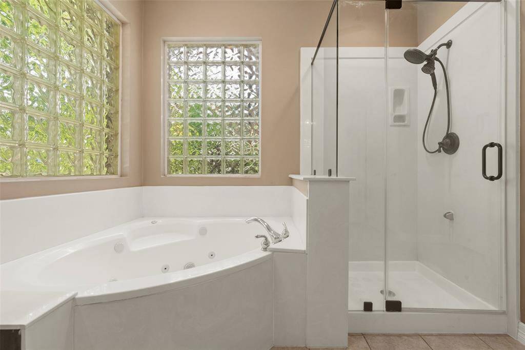 Primary bathroom features a luxurious corner jacuzzi tub and a separate glass-enclosed shower, complemented by large glass block windows for natural light and privacy.