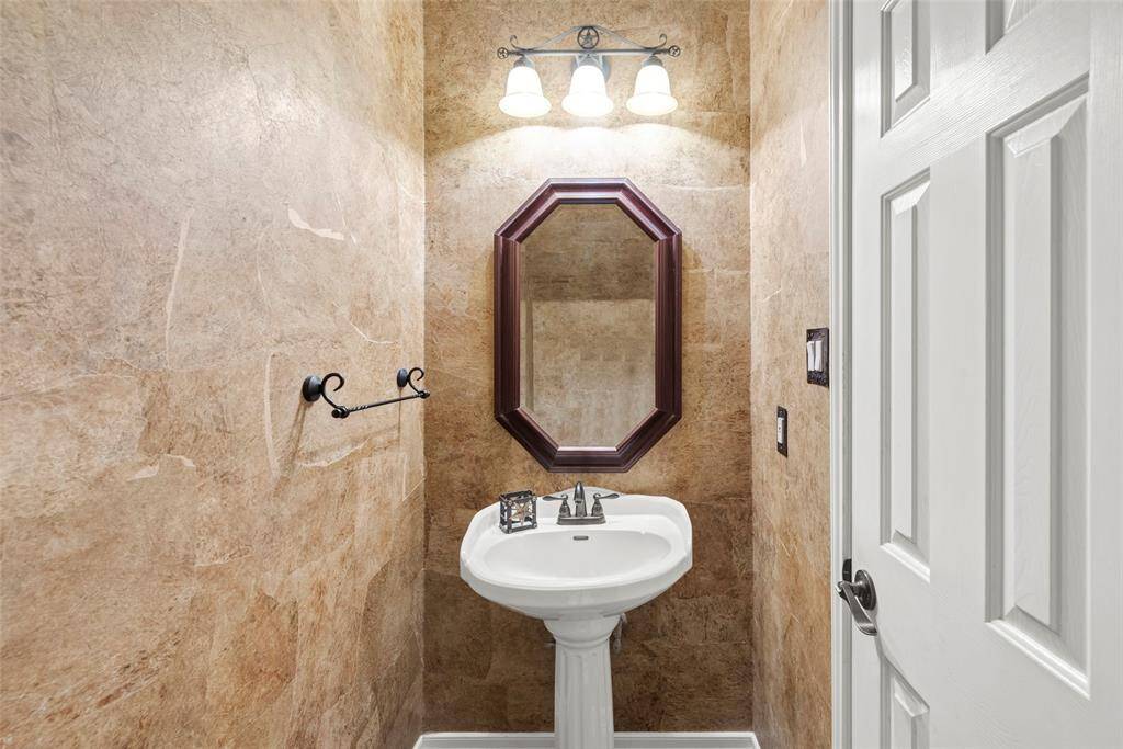 This is a cozy powder room featuring a pedestal sink, octagonal mirror, and warm-toned walls. It has a classic light fixture above the mirror and a towel holder beside the sink.