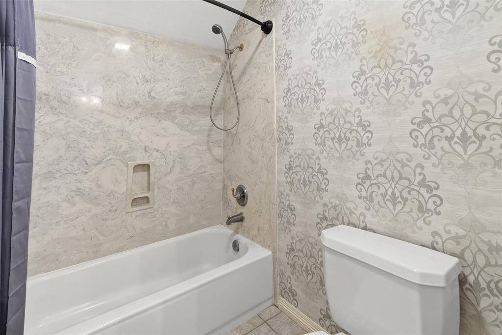 Bathroom has classic design with a bathtub and shower combo, elegant marbled wall tiles, and a decorative patterned accent wall.