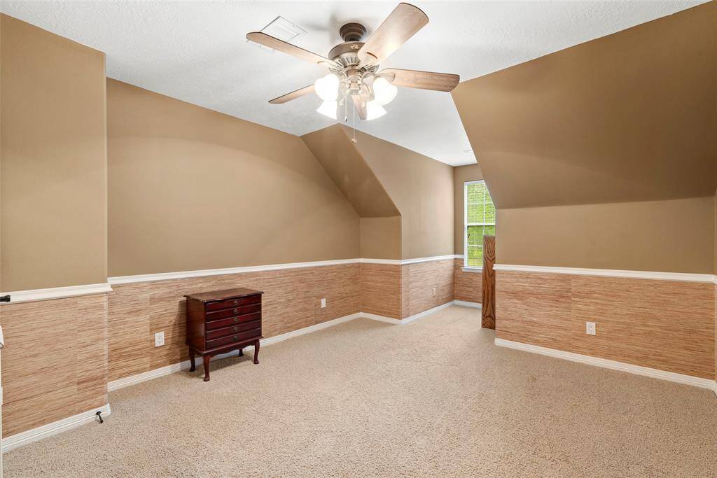 Third upstairs room features a cozy, carpeted space with tan walls and a white trim. It includes a ceiling fan with lights and a window for natural light. The room's design is simple and functional, suitable for multiple uses.