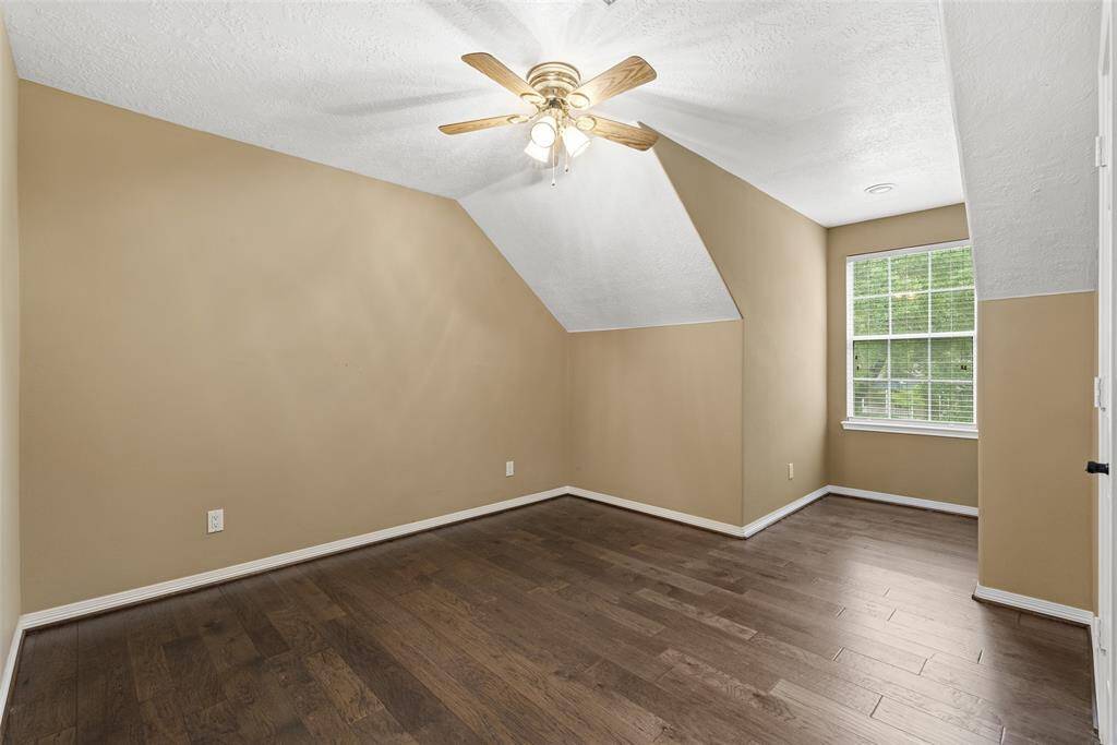 This room features a cozy space with angled ceilings, neutral beige walls, and dark wood flooring. It includes a ceiling fan for comfort and a window providing natural light. Perfect for a bedroom or office.