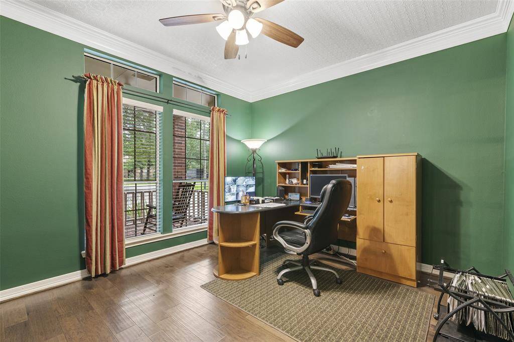 This home office features rich green walls and hardwood flooring. It includes a large window with a view, a ceiling fan, and a cozy workspace with wooden furniture, making it both functional and inviting.
