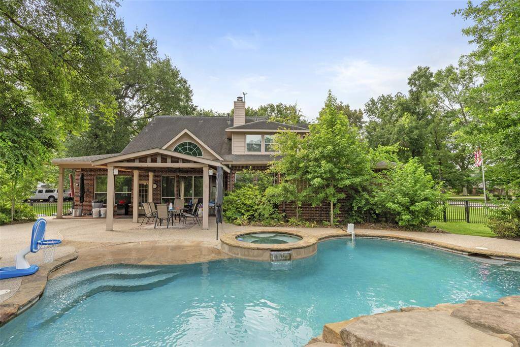 Backyard has a refreshing pool and hot tub, complemented by a covered patio area perfect for outdoor dining and relaxation. The brick exterior and surrounding greenery provide a serene and private atmosphere.