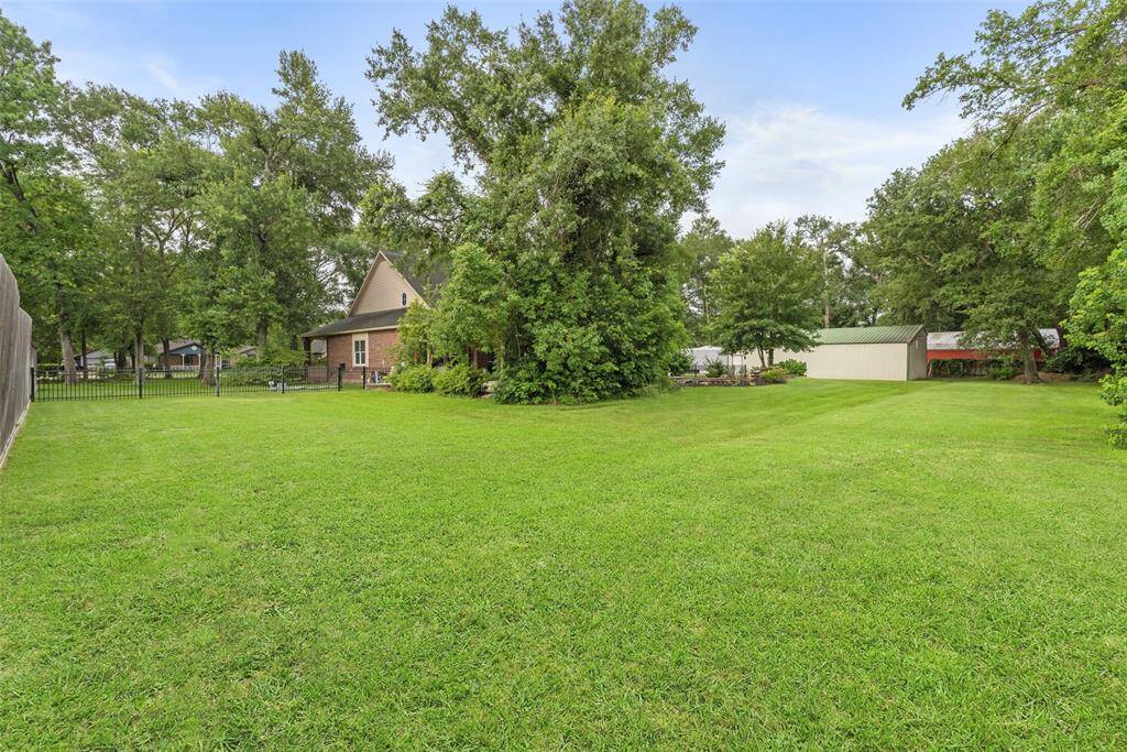 Spacious backyard with lush green lawn and mature trees, offering privacy and ample space for outdoor activities. A charming brick house is partially visible, surrounded by nature. Ideal for those seeking a serene and expansive outdoor area.