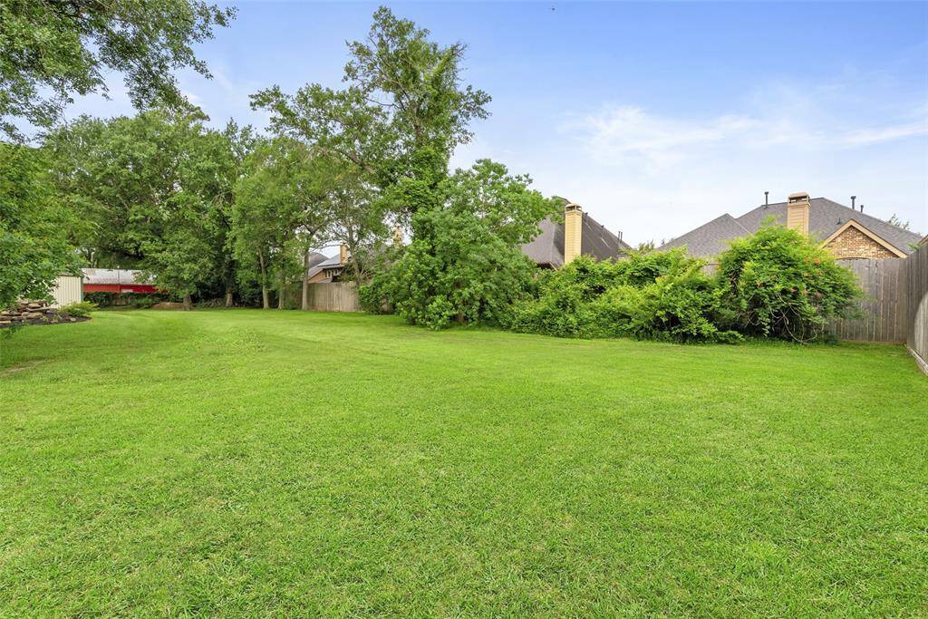 Spacious, lush green backyard with mature trees and privacy fencing, ideal for outdoor activities and relaxation.