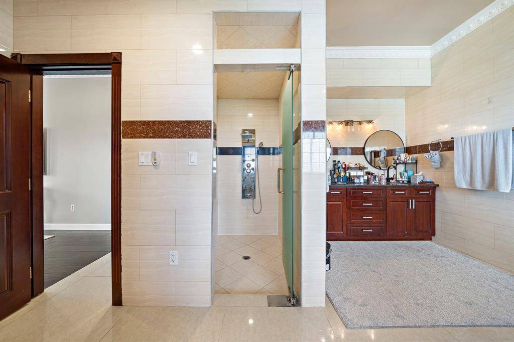 Primary shower with opaque glass door and shower system with handheld shower head.