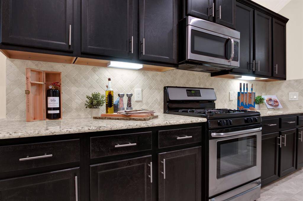 This modern kitchen features sleek black cabinets, stainless steel appliances, and a tiled backsplash. The granite countertops provide ample workspace, and under-cabinet lighting adds a warm touch.